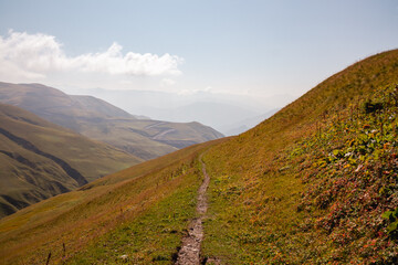 A hiking trail over the Chaukhi Pass leading through grassland in the Greater Caucasus Mountain Range in Georgia, Kazbegi Region. The surrounding mountains and hills are green and soft. Tranquility.