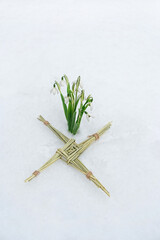 Brigid's cross and snowdrops flowers in snow. symbol of Imbolc sabbat. ireland handmade amulet made from straw. Wiccan tradition for blessed, protected house. spring and winter pagan festive ritual. - obrazy, fototapety, plakaty