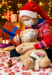 Child girl as Santa helper posing in new year decoration. Wearing a protective face mask against viruses, coronaviruses. She plays with a toy bear, treats him, gives injections