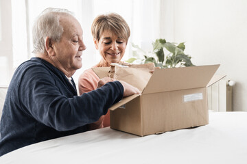 Happy senior couple unpacking parcel box from online delivery service - Focus on woman face - Powered by Adobe