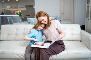 mother and daughter looking a book with photos from a family photo shoot - obrazy, fototapety, plakaty