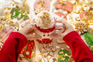 Fototapeta premium Banner for Christmas and New Year gingerbread cookies snowflakes, Santa hat, Christmas trees, garlands on red silk fabric background and mug with hot chocolate and cream in child hands
