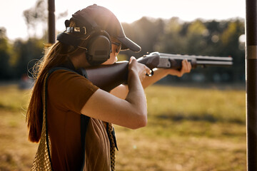 Young redhead caucasian woman on tactical gun training classes. Woman with weapon. Outdoor Shooting...