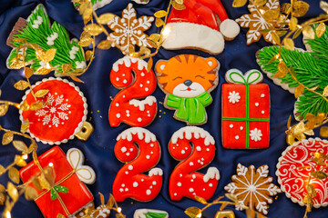 Banner for Christmas and New Year gingerbread cookies numbers 2022, snowflakes, Santa hat, Christmas trees, garlands on blue silk fabric background, gingerbread tiger symbol Chinese zodiac calendar