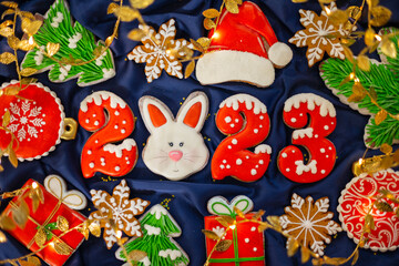 Banner for Christmas and New Year gingerbread cookies numbers 2023, snowflakes, Santa hat, Christmas trees, garlands on blue silk fabric background, gingerbread rabbit symbol Chinese zodiac calendar
