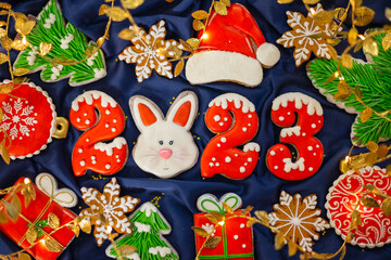 Banner for Christmas and New Year gingerbread cookies numbers 2023, snowflakes, Santa hat, Christmas trees, garlands on blue silk fabric background, gingerbread rabbit symbol Chinese zodiac calendar