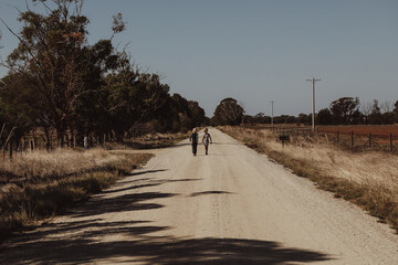 Little boys walking together on lonely country road surrounded by dry fields