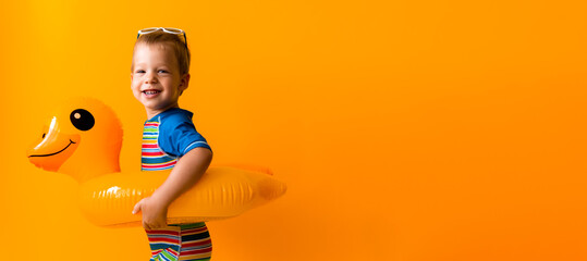 banner happy little smiling child swimmer sport boy wear sun glasses swimsuit, Kid Inflatable swimming ring yellow duck point to side away, isolated orange background. hot summer vacation copy space