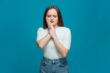 Young sad unhappy girl suffer toothache, pain from sensitive tooth on blue background. Dental...