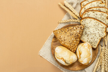 Freshly baked bread with wheat ears, buns, and toasts. Assorted bakery on light beige background