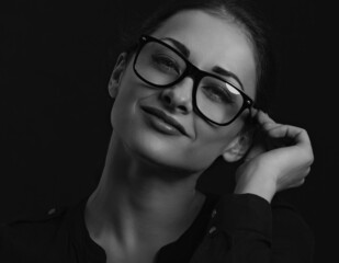 Fototapeta na wymiar Beautiful thinking business woman looking happy in eye glasses and holding spectacles in casual black t-shirt on black background with empty copy space. Closeup
