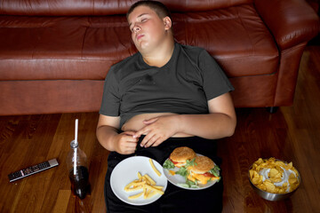 overeat boy sleep on floor in living room, young caucasian teen boy fall asleep while he was...