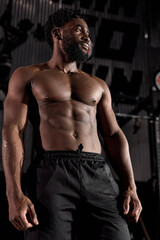 Obraz na płótnie Canvas Portrait of serious muscular male with naked torso posing standing after workout in gym, looking confident and motivated. handsome guy with beard wearing black shorts looking at side