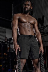 Fototapeta na wymiar Heavy ropes training. portrait of african american muscular man in workout gear going to exercising with battle ropes at the gym cross training motivation challenge improvement achievement strength