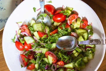 Vegetable salad of fresh herbs, sliced tomatoes, tomatoes, cucumbers, seasoned with natural olive oil in a white deep bowl bowl view above. A healthy dietary homemade meal flatly. Rural simple food.