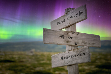 find a way or make one text quote on wooden signpost outdoors in nature with northern lights above.