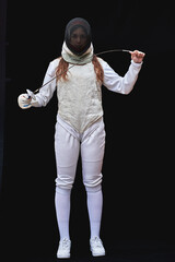 Portrait of a young fencer wearing white fencing costume and mask and holding the sword in front of...