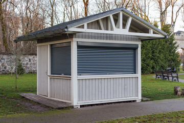 Closed wooden kiosk in the park. The windows are closed with iron blinds