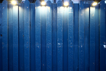 Blue wooden fence. Four spotlights are shining.