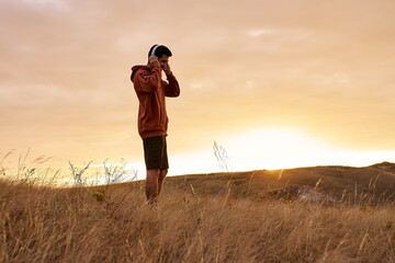 Enjoy life. Man Stand on mountain field enjoying the sunrise, listening to music in headphones....