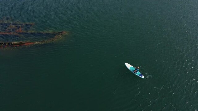 Aerial shot. Young women is having fun. Stand Up Paddling in the sea. SUP. Paddling among debrees of a sunk metal ships