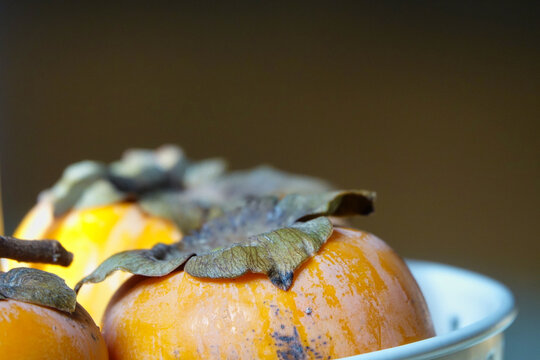Detail of some ripe kakis in a fruit bowl indoors illuminated by natural light
