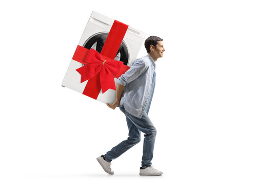 Full length profile shot of a casual young man carrying a washing machine with a red ribbon bow on his back