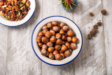 Enameled metal bowl filled with raw hazelnuts in their shell