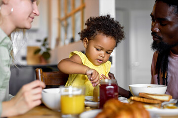 adorable black toddler girl enjoying Breakfast with parents at home, pretty child eating porridge....
