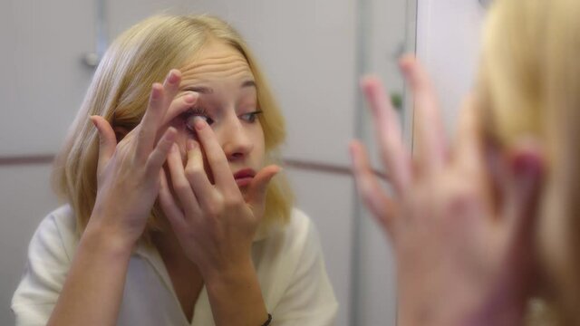 teenage girl blonde puts on contact lenses in front of a mirror.