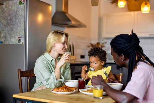 Quality time with great food. Family with child in kitchen eating together. In the morning at weekend, have meal, mother father and daughter. diverse parents and kid girl with dark skin - Powered by Adobe