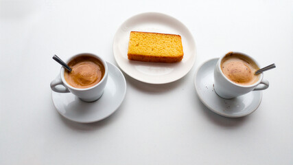 Two cups of coffee latte, teaspoons, saccharin and a sponge cake seen from above on a white table
selective focus
