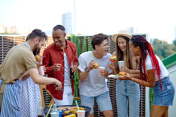 International diverse friends eating burgers and drinking lemonade at barbecue patio party. Cheerful excited people having fun at bbq lunch. Youth lifestyle, summer and friendship concept. Portrait
