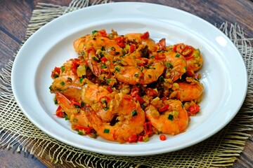 Stir fried prawns with chilli garlic and salt in white plate on wooden table. Thai seafood.