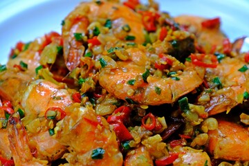 Stir fried prawns with chilli garlic and salt in white plate on wooden table. Thai seafood.