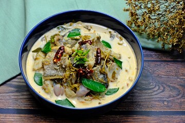 Snakeskin gourami and young tamarind leaf in coconut milk in dark blue bowl n wooden table. Authentic Thai food.