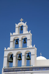 Traditional Greek white church with cross and bells in village Oia on Santorini, Greece. Oia is a small town and former community in the South Aegean on the islands of Santorini.