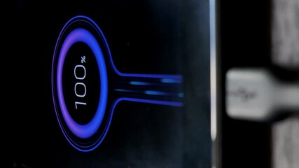 displaying 100 percent of the battery charge on the display of a mobile phone. mobile phone on a wooden table.vertical screen