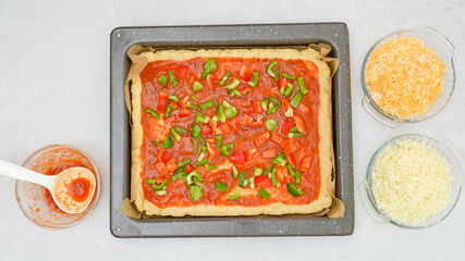Homemade vegetarian pizza recipe. Pizza dough with tomato sauce and fresh chopped vegetables close up on baking pan, flat lay
