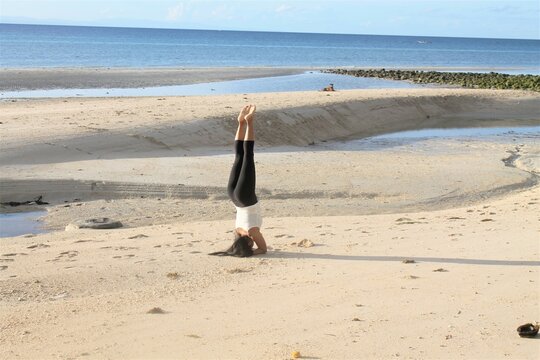 The person is doing a yoga headstand at the beach.