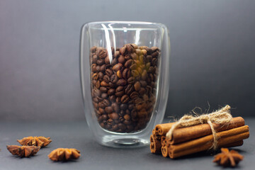 Transparent coffee cup full of coffee beans on the grey background.