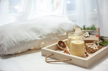 Two glasses of eggnog on a tray of Christmas presents in bed. Christmas breakfast. Sweet winter egg dessert.