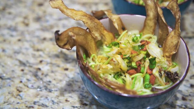 Closeup of female woman hands arranging raw vegan cooking of soup with water broth and dehydrated vegetables, celery and oyster mushrooms dried and marinated for healthy dish