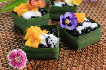 Homemade Coconut Black Sticky Rice with Mango in Pandan Leaves Cup, Selective Focus with Pansies Edible Flower Topping