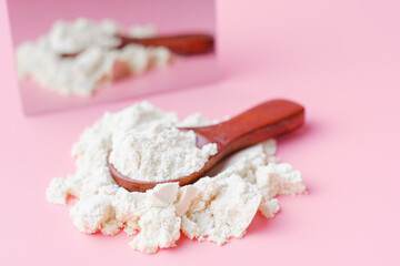 Wooden spoon with protein or collagen powder on pink background close-up.