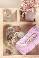 Lilac-colored towel, bottle of dry herbs on a wooden tray.  Herbal spa, Body care, flat lay