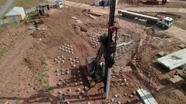 A large vertical pile-driving crane hammers reinforced concrete piles into the ground at a construction site.