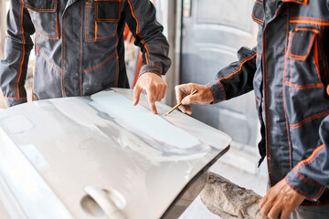 Two workers discuss the execution of the work of Repairing car body, Application putty close up. The mechanic repair the car. Work after the accident by working sanding primer before painting. - 471635327