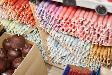 Many multicolored colorful paraffin stick Pastel colors candles arranged in shelves lying on shelter and sorted by color in a household candle shop store market.