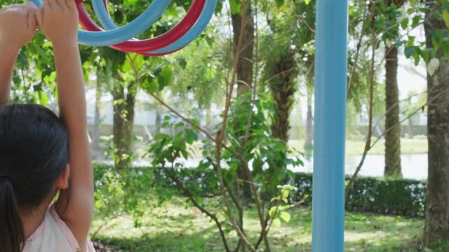 Happy little girls having fun on colorful bar at outdoor playground. Active kid hang on colorful monkey bars in the park. Play is learning in childhood.